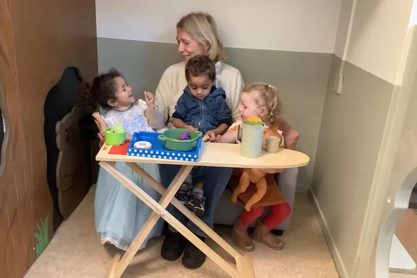 Ilonka zit met peuters in de poppenhoek